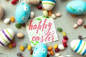 Happy Easter concept. Preparation for holiday. Easter eggs Inscription HAPPY EASTER letters candy chocolate eggs and jellybean sweets on concrete stone grey background. Flat lay top view copy space. photo