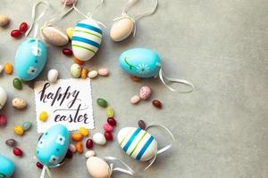 Happy Easter concept. Preparation for holiday. Easter eggs Inscription HAPPY EASTER letters candy chocolate eggs and jellybean sweets on concrete stone grey background. Flat lay top view copy space. photo