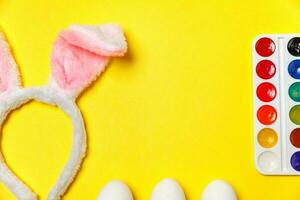 Decorative eggs colorful paints and bunny ears furry costume toy isolated on trendy yellow background photo