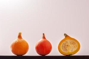 One red pumpkin, one yellow and one cut with seeds inside, lie in a row against a white background. Red pumpkin in the center. Copy space. photo