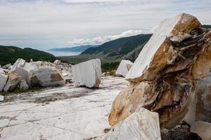 Large white marble blocks in an old abandoned quarry on the background of hills and Lake Baikal. Smooth cuts at the stones. Cloudy. Horizontal. photo