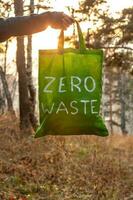 Zero waste concept. Textile green bag with a white inscription in hand on a background of nature and the sun. photo