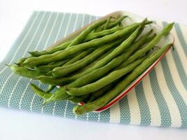 Fresco verde frijoles en un rectangular plato con un azul paño debajo foto