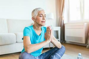 Senior woman in the prayer position . Woman practicing yoga, relaxing in prayer position on mat. Elderly woman wearing sportswear working out, meditating in yoga studio or at home photo