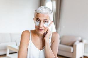 beauty, skin care and old people concept - portrait of smiling senior woman with hydrogel under-eye patches touching her face photo