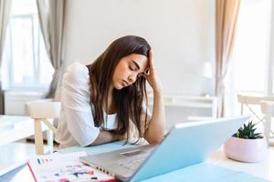 Young frustrated woman working from home office in front of laptop suffering from chronic daily headaches, treatment online, appointing to a medical consultation, electromagnetic radiation, sick pay