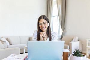 mujer joven feliz con auriculares hablando mirando la computadora portátil tomando notas, estudiante hablando por videoconferencia, profesora tutora por cámara web, capacitación en línea, concepto de entrenamiento electrónico foto