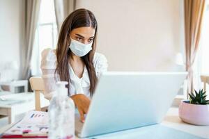 Quarantine, remote job and pandemic concept - woman wearing face protective medical mask for protection from virus disease with laptop computer having video call at home office photo