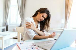 Young woman with hands holding her shoulder pain. Office syndrome and Health care concept. Business woman working with her laptop and with shoulder pain in the home office photo
