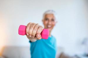 Senior woman exercising with dumbbells at home. Sporty beautiful woman exercising at home to stay fit. Elderly woman exercising at home in a living room. Fitness, workout photo