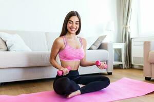 Young woman exercise with dumbbells at home and watching tutorial lesson on laptop computer. happy young female doing arm workout using dumbbells and looking at tutorial on her laptop photo