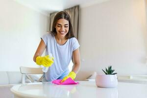 mujer vistiendo amarillo caucho protector guantes y limpieza blanco mesa. contento hembra ama de casa limpieza el casa foto