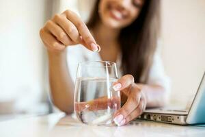 Closeup of a young woman dropping an effervescent antacid in a glass of water. young woman hardly put a soluble pill with a medicine for pain or a hangover in a glass of water photo