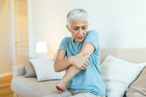 vejez, problema de salud y concepto de personas - cerca de una anciana que sufre de dolor en la mano en casa. mano de mujer sosteniendo su codo que sufre de dolor en el codo. foto