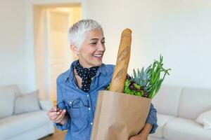 Healthy positive happy senior woman holding a paper shopping bag full of fruit and vegetables. portrait of a middle aged woman holding the purchase photo