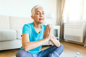 Senior woman in the prayer position . Woman practicing yoga, relaxing in prayer position on mat, Padmasana exercise, elderly woman wearing sportswear working out, meditating in yoga studio or at home photo