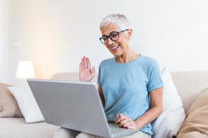 Progressive pensioner. Clever enthusiastic progressive senior woman waving her hand and feeling happy while using a video call in her laptop and talking with grandchildren photo