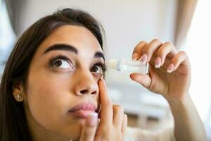 visión y oftalmología medicamento. de cerca de hermosa mujer aplicando gotas para los ojos en su ojos. joven hembra modelo con natural maquillaje utilizando un botella de ojo gotas. salud concepto. alto resolución foto