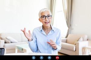 Cheerful mature woman having a video call from home, Online business concept. Senior woman explaining with her hands photo