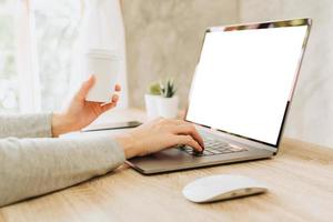 woman using laptop and holding coffee working on wooden table photo