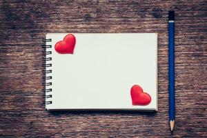 Blank notebook and red heart with pencil on wood background with space. photo