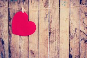 Red heart hanging on clothesline and rope with wooden background photo