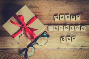 Happy father's day block and gift box with glasses on wood background. photo