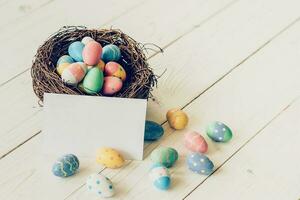 vistoso Pascua de Resurrección huevos en el nido y papel tarjeta en madera mesa antecedentes. foto