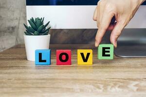 mano sostener de madera cubo con texto amor en mesa foto