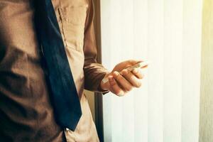 Young business man holding smartphone in the office with sunlight. Vintage toned filter. photo