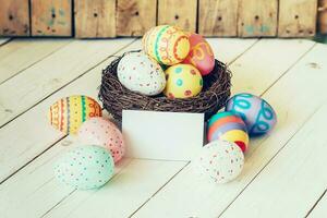 Colorful easter eggs in the nest and paper card on wood table background. photo