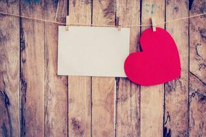 Red heart hanging and paper on clothesline and rope with wooden background photo