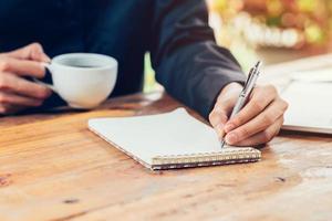 Asia hombre mano escritura cuaderno papel en madera mesa en café tienda con Clásico tonificado filtrar. foto