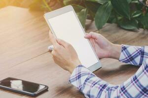 Close up hand woman holding tablet blank screen display on wood table with sunlight. Vintage toned. photo