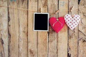 Two heart and photo frame hanging on clothesline rope with wooden background.