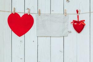 Red heart and old paper blank hanging at clothesline on wood white background with space. Valentine Day. photo