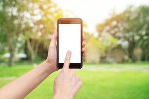 Hand holding phone with defocused bokeh and blur background of garden trees in sunlight. photo