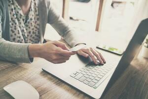 Asian woman holding credit card paying for shopping in computer laptop on wooden table photo