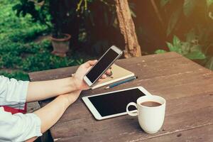 Woman hand holding phone and blank screen display on wood table in coffee shop. photo