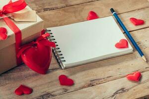 Blank notebook and gift box with red heart on wood background. photo