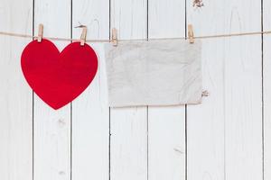 Red heart and old paper blank hanging at clothesline on wood white background with space. Valentine Day. photo