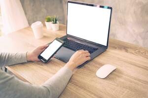 Hipster women holding phone and using laptop on wooden table in coffee shop. photo