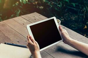 Woman hand holding tablet and blank screen display on wood table in coffee shop. photo