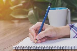 Close up hand woman writing notebook on wood table with sunlight. Vintage toned. photo