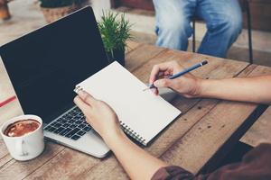 Young business man hand writing notebook and using laptop on wood table. photo