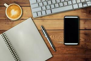 Mobile phone, notebook pen, keyboard computer and coffee cup on office wooden table with copy space. photo