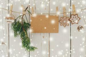 Close up of christmas decoration and blank paper card with snow hanging on wood background.