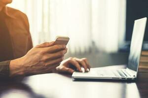 Young business man hand holding and using smartphone in the office with sunlight. Vintage toned filter. photo