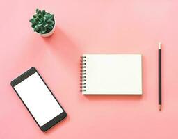 Flat lay mockup design of workspace desk with blank notebook, smartphone, coffee, stationery on pink pastel color with copy space photo