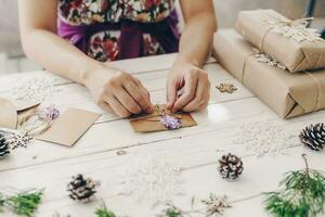 Close up of hands holding wrapping gift box and christmas card on wooden table with xmas decoration. photo